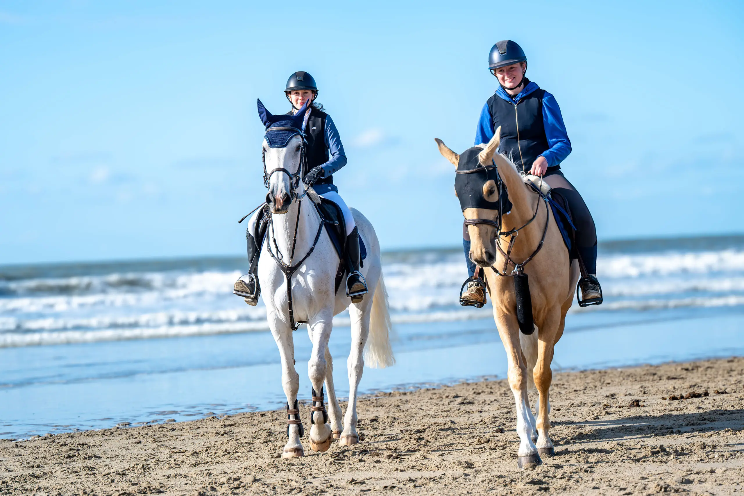 Twee ruiters op een schimmel en een palomino op het strand